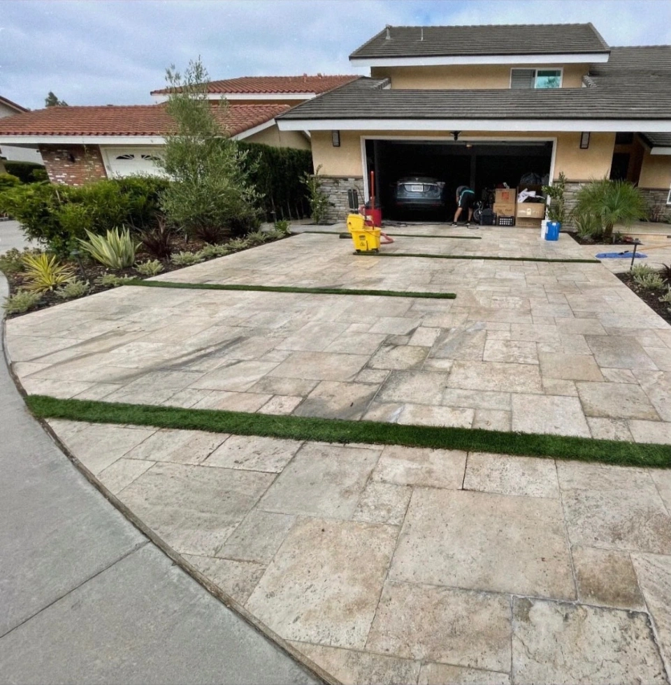 The same travertine driveway before cleaning, stained and streaked with the crew's equipment still on it
