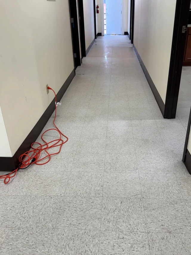 The same office corridor before the work, with flat, scuffed tile and no shine
